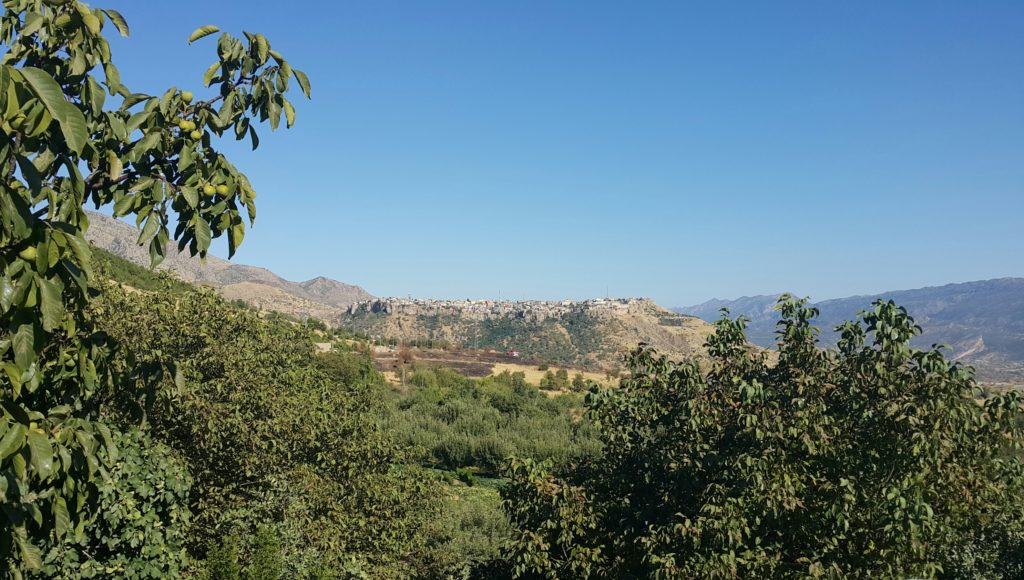 Image illustrating the city of Amedy viewed from a distance. A settlement appears on top of a low mound