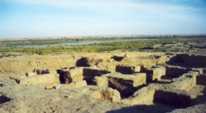 image illustrating the archaeological ruins of ashur in iraq. mudbrick remains of a building appear in the foreground. the river tigris appears in the background