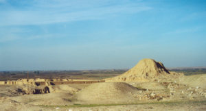 image illustrating the archaeological site of ashur in Iraq. a high mound appears to the right, with other mudbrick remains in the foreground and left