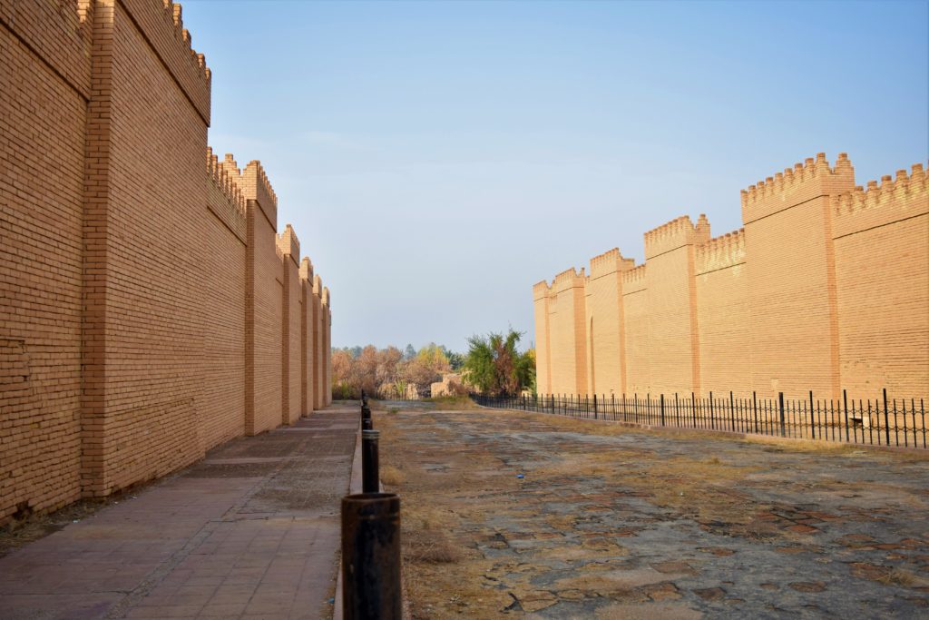 image illustrating the reconstructed processional way at the archaeological site of babylon in iraq. brick walls in neo-babylonian style appear on each side of a paved way